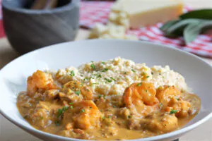 Shrimp in a creamy sauce served with cheesy grits and parsley in a white bowl.