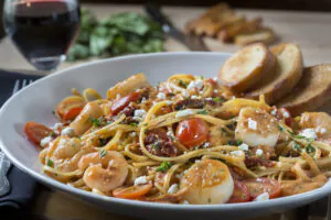 Seasoned shrimp and sea scallops sautéed with garlic, grape tomatoes and basil. Tossed with fresh linguini in a sun-dried tomato scampi sauce finished with crumbled goat cheese.